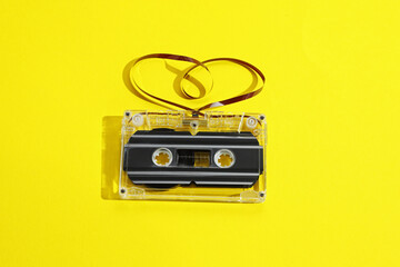 One audio cassette with heart shaped magnetic tape on yellow background, above view