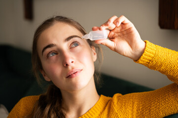 Portrait of a calm young woman putting eye drops in the living room, female feeling eye fatigue and...