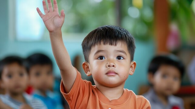Smart asian boy raising his hand enthusiastically to answer a teacher's question in an elementary school classroom, demonstrating eagerness to learn and actively participate in lessons