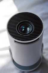 modern white portable projector standing on a soft fabric surface in natural light. concept of home cinema, entertainment technology, and minimalist design.