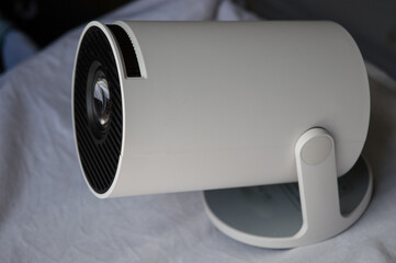 modern white portable projector standing on a soft fabric surface in natural light. concept of home...