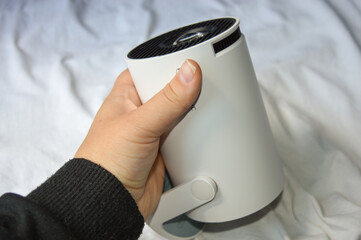 modern white portable projector standing on a soft fabric surface in natural light. concept of home...