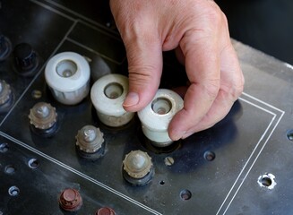 Close-up shot of a worker hand screwing a white ceramic plug fuse into an old black electrical panel
