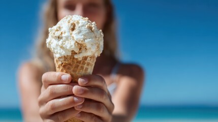 Delight in the refreshing experience of enjoying a delicious ice cream cone, held in front of a beautiful beach setting, perfect for summertime relaxation.
