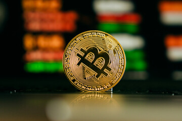 A shiny golden Bitcoin stands upright on a keyboard, symbolizing digital currency, blockchain...