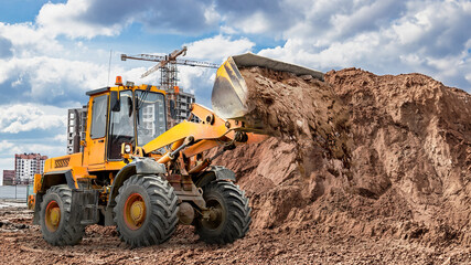 Fototapeta premium Heavy machinery moves dirt at construction site under cloudy sky in urban environment