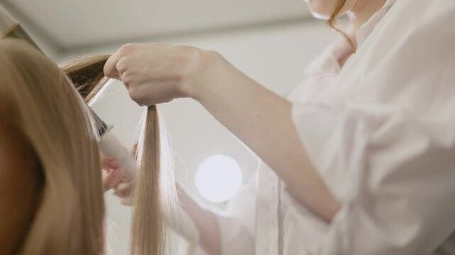 Hair curling. Caucasian woman makeup artist hairdresser stylist curling hair with curling iron, creating curls. Close-up