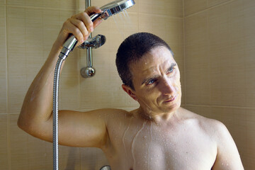 Routine moments of daily life: mature man standing under the shower, holding the shower head over...