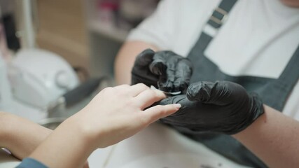 Nail technician in black glove gently cleaning client hand with wipe during manicure session, showing care and precision in professional nail salon environment with visible equipment in background