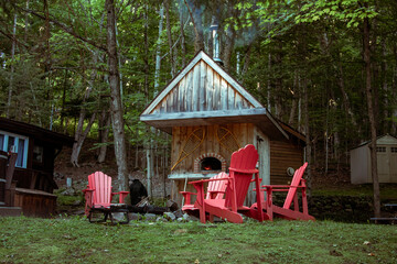 Wooden chairs in front of log fire pit and wood fired pizza oven in Algonquin Ontario