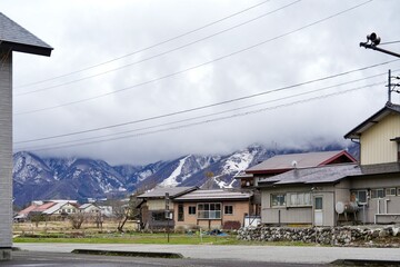 Japanese village with snowy mountains and low-hanging clouds,peaceful rural landscape in Japan.