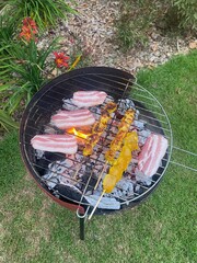 Bacon and other meat starting to get cooked in a domestic barbecue on a green garden