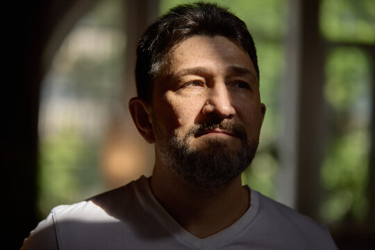 Emotional depth. Contemplative older man with a thoughtful expression stands in soft window light. Concept of introspection and peaceful reflection in natural lighting. - Powered by Adobe
