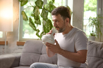 A middle aged Caucasian man is using a home inhalation device for respiratory therapy indoors....