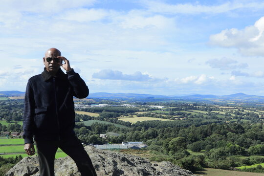 Confident Man Overlooking Enniscorthy Town from Vinegar Hill Summit, County Wexford, Ireland on a Bright Sunny Evening &ndash; Panoramic Hilltop View with Lush Green Fields and Rolling Hills