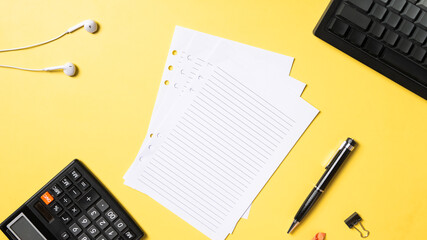 Flat lay of office desk items including lined paper, pen, keyboard, calculator, earbuds, and a...