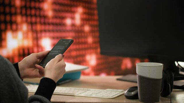 Time laps. A programmer at office desk holding mobile phone and typing on it