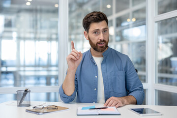 A businessman gestures while talking, offering a clear point or idea. He is in an office setting.