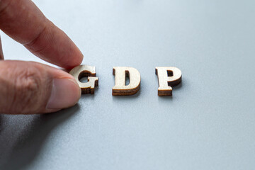 A finger adjusting wooden block letters that spell out "GDP". Gross Domestic Product, economic measurement, growth, data analysis, nation's economy concept.