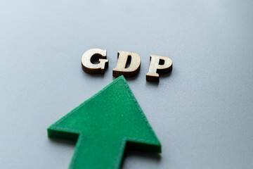A green arrow points upwards, with wooden block letters spelling "GDP". Economic growth, an increase in Gross Domestic Product, prosperity, and positive financial trends for a nation concept.
