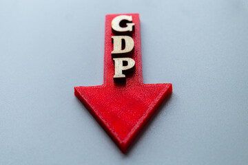 A red arrow points downwards, with wooden block letters spelling "GDP". Decline in Gross Domestic Product, economic contraction, recession and financial downturn concept.