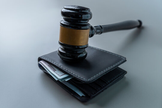A judge's gavel on a wallet overflowing with US hundred-dollar bills. Wage garnishment, fines, legal fees concept.