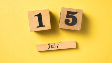 Wooden calendar blocks display the date July 15 against a bright yellow background. A simple flat...
