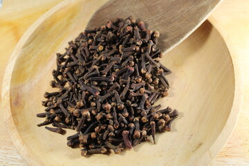 dried cloves rests on a wooden spoon, spilling onto wooden plate, ready for culinary use