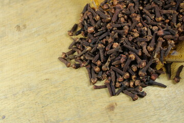 A close-up shot of dried cloves spilling from a glass container onto a rustic wooden surface,...