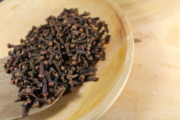 dried cloves rests on a wooden spoon, spilling onto wooden plate, ready for culinary use