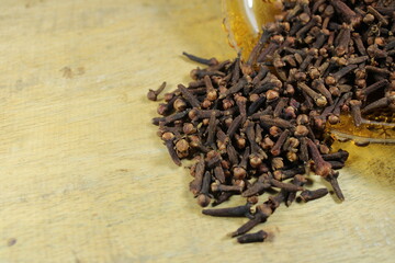 A close-up shot of dried cloves spilling from a glass container onto a rustic wooden surface, highlighting their aromatic texture