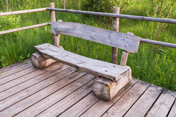 Naklejka premium Rustic handmade wooden bench on a boardwalk in a park. A tranquil spot for rest and solitude surrounded by lush greenery.