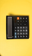 A black 12-digit office calculator on a solid yellow background, showing various function keys and a clear digital display in a top-down layout