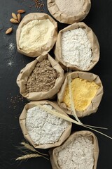 Different types of flour in paper bags on black table, flat lay