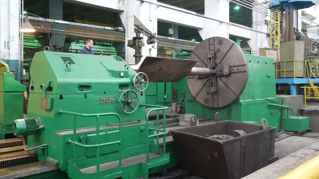 A large metal part rotates on a milling machine in the workshop of a heavy industry plant. Industrial production and metalworking process. 