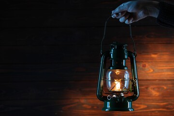 Woman holding vintage kerosene lantern near wooden wall, closeup. Space for text