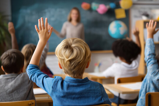 Happy elementary students raising their hands on a class at school.