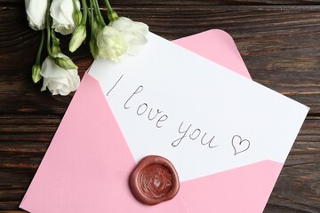 Letter with phrase I Love You, envelope and beautiful flowers on wooden table, flat lay
