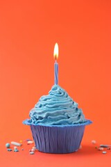 Burning candle in cupcake and sprinkles on orange background