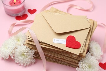 Stack of letters with phrase I Love You, flowers, burning candle and red hearts on pink background,...