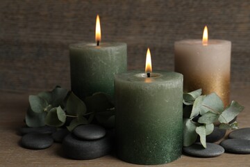 Burning candles, stones and eucalyptus branches on wooden table, closeup