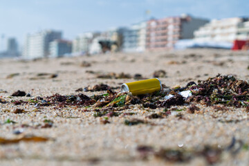 Yellow can polluting a beach with seaweed and buildings in the background