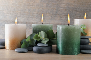 Burning candles, stones and eucalyptus branches on wooden table, closeup