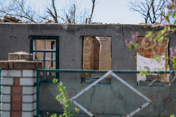 A completely destroyed house stands with only its frame and crumbling walls remaining, situated in...