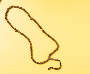 A wooden prayer bead string (tasbih) arranged on a bright yellow background. A spiritual accessory...