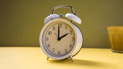 A classic white twin-bell alarm clock showing 10:00, placed neatly on a bright yellow background...