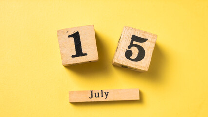 Wooden calendar blocks display the date July 15 against a bright yellow background. A simple flat lay design highlighting a mid-year date in a bold and minimal style