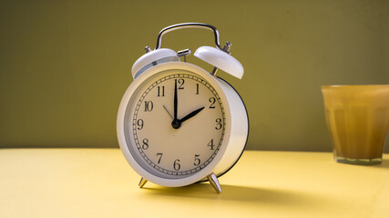 A classic white twin-bell alarm clock showing 10:00, placed neatly on a bright yellow background...