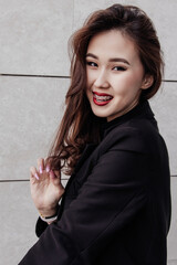 A smiling woman with braces poses in a black blazer against a modern wall
