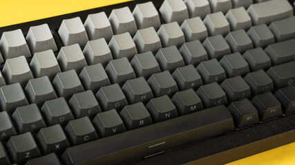 Fototapeta premium Minimalist mechanical keyboard with gradient gray keycaps placed on a vibrant yellow background, showcasing a clean, modern, and top-down tech aesthetic